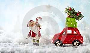Santa Claus and red toy car carrying Christmas gifts in snowy la