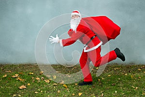 Santa Claus runs with a big red bag with gifts.