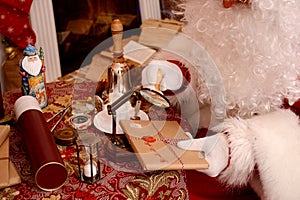 Santa Claus sealing a letter, looking through magnifier glass