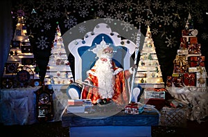 Santa Claus is sitting in a chair at his night residence and reading Christmas letters