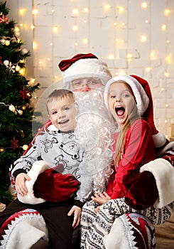 Santa Claus sitting with happy little kids cute children boy and girl near Christmas tree