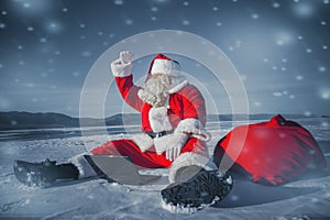 Santa Claus sitting in the snow with a laptop and looking away