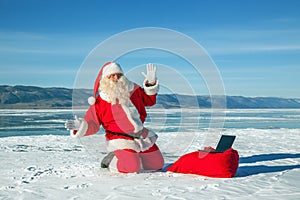 Santa Claus sitting on snow, looking at laptop news