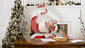 Santa Claus sitting at the table in his Christmas workshop signing presents for children