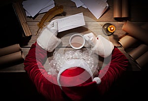 Santa Claus sitting at the table in his room and reading Christmas letter from child