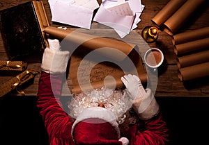 Santa Claus sitting at the table in his room and reading Christmas letter or wish list