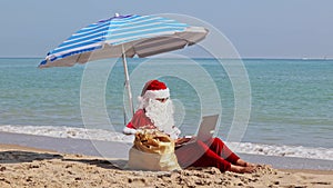 Santa Claus sitting under an beach umbrella at sea on a hot summer day