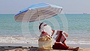 Santa Claus sitting under an beach umbrella at sea on a hot summer day