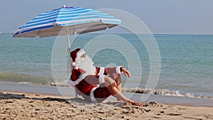 Santa Claus sitting under an beach umbrella at sea on a hot summer day