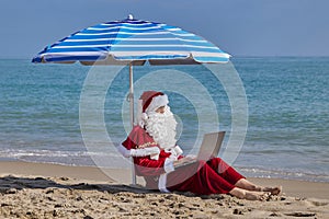 Santa Claus sitting under an beach umbrella at sea on a hot summer day