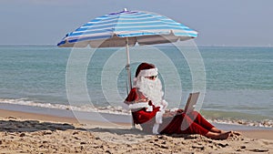 Santa Claus sitting under an beach umbrella at sea on a hot summer day