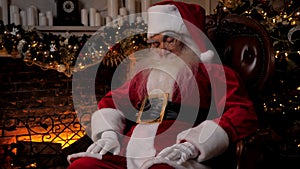 Santa Claus sleeping sitting on chair on background fireplace Christmas tree