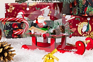 Santa claus on sleigh, lollipop staff, boxes with gifts, christmas tree cone and golden bell on a background of snow