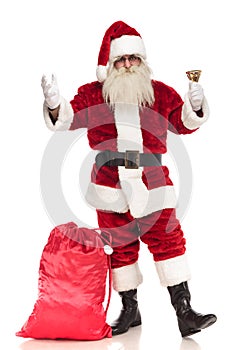 Santa claus standing with sack near leg rings his bell