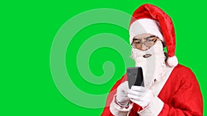 Santa Claus standing uses a smartphone and Internet applications, isolated on green background.