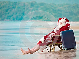 Santa Claus with a suitcase and resting on the beach barefoot