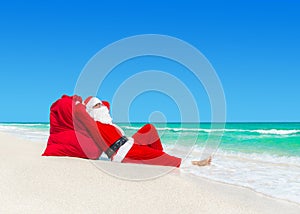 Santa Claus sunbathe on Christmas gifts sack at ocean beach