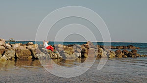 Santa Claus sunbathes. Santa Claus having fun. Funny Santa, in sunglasses and flippers sitting on rocky beach by the sea