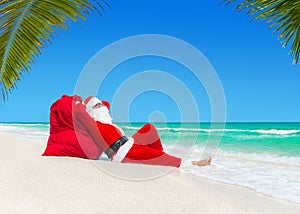 Santa Claus sunbathing on Christmas gifts sack at ocean palm bea