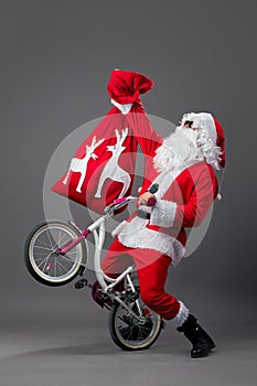 Santa Claus in sunglasses and headphones puts the bike on the back wheel and hold in the hand the bag with Christmas