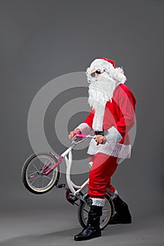 Santa Claus in sunglasses and headphones puts the bike on the back wheel on the white background.