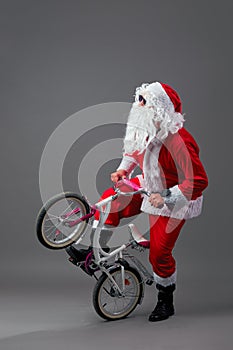 Santa Claus in sunglasses and headphones puts the bike on the back wheel on the white background.