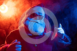 Santa claus in sunglasses in red-blue smoke. Party for Christmas.