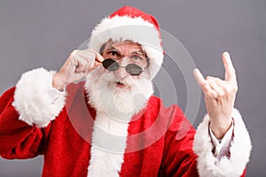 Santa Claus In The Sunglasses Standing And Showing A Rock Gesture