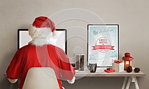 Santa Claus surfs the web on laptop. On his table is lantern, picture, gifts, books and a cup of hot tea