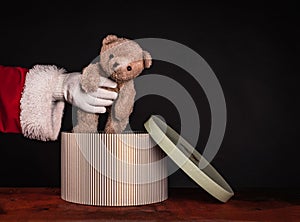 Santa Claus takes out a cute teddy bear from a gift box