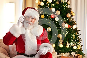 Santa Claus talking by mobile phone in room decorated for Christmas