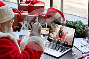 Santa Claus talking to child on laptop video call open present sit at table.