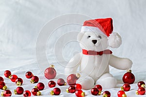 Santa claus teddy bear eyes who wearing hat sitting with red Christmas baubles