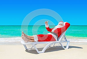 Santa Claus thumbs up gesturing on sunlounger at tropical beach