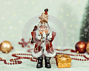 Santa Claus toy brings Christmas tree at blue snowy night bokeh background and blurred lights foreground.