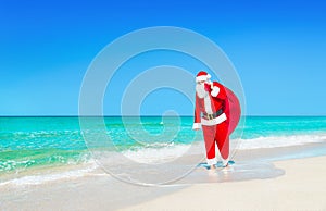 Santa Claus walks with large Christmas gifts sack at ocean beach