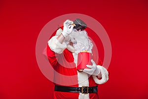 Santa Claus wearing virtual reality goggles and a red bucket with popcorn, on a red background. Christmas