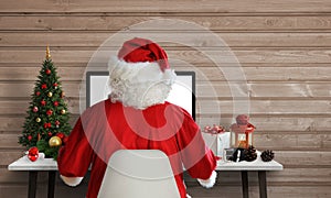 Santa Claus work on a computer in his office. Answer on letters and greeting cards via email