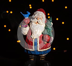 Santa clause figurine with blue bird on hand and a pine tree in the other hand. light points in the black background