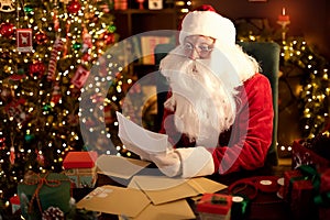 Santa Clause is prepares gifts for children for Xmas at his desk at home while reading wish lists