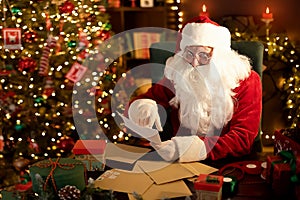 Santa Clause is prepares gifts for children for Xmas at his desk while reading wish lists at home