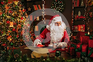 Santa Clause preparing for Christmas packing gifts while sitting at the table. New Year concept