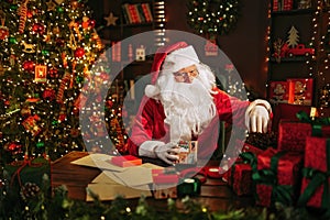 Santa Clause preparing for Christmas packing presents while sitting at the table. New Year concept