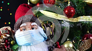 Santa clouse with face mask next to Christmas tree with blinking lights