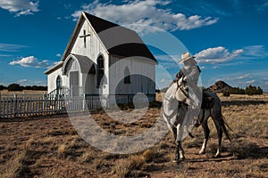 Cowboy rests his horse in front of an old church in rural area of New Mexico.