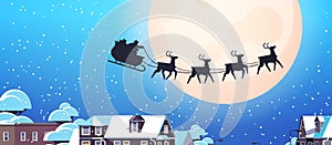 Santa flying in sledge with reindeers in night sky over village houses happy new year merry christmas banner