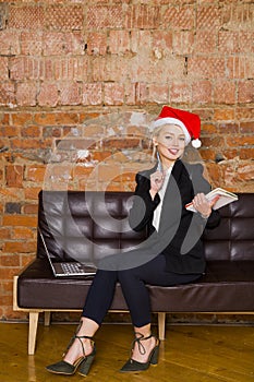 Santa girl businesswoman with notebook and laptop at loft office on leather couch in suit. Business concept.