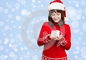 Santa girl holding christmas gift over holidays lights background. Young happy woman in santa hat showing Christmas present. Beau
