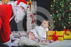 Santa and girl playing near fireplace, decorated Christmas tree