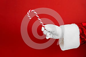 Santa hand with Christmas candy cane on red background. Merry Christmas sweets and Happy New Year concept